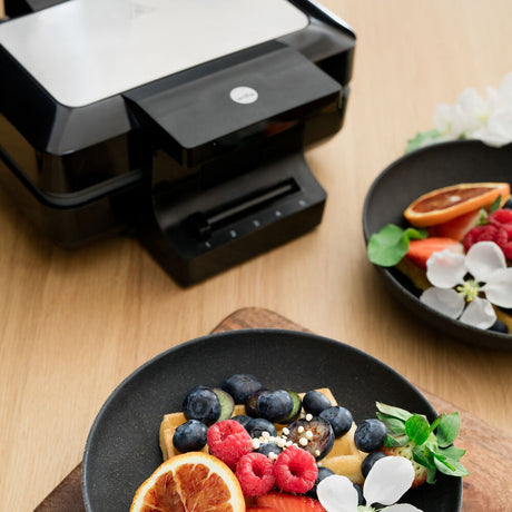 A sleek black GAUFRES BELGIAN with silver accents is pictured against a white background. A gold and black badge with the text "TESTVINNER" is displayed in the top left corner, indicating it has been awarded a test winner. The waffle maker features adjustable temperature and double release coating for perfect waffles every time.